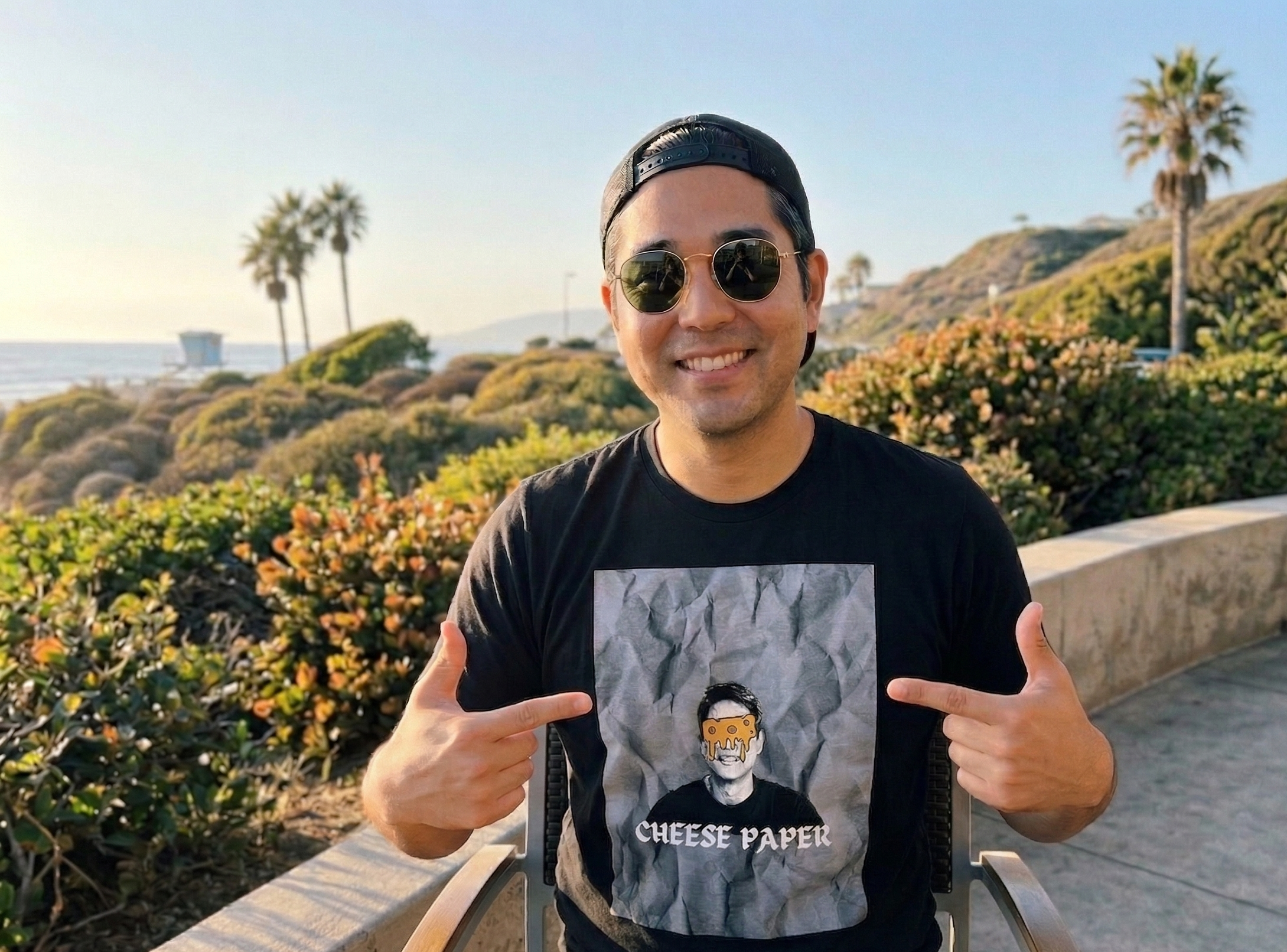 man with cheese paper pointing at his t shirt on top of a view in california