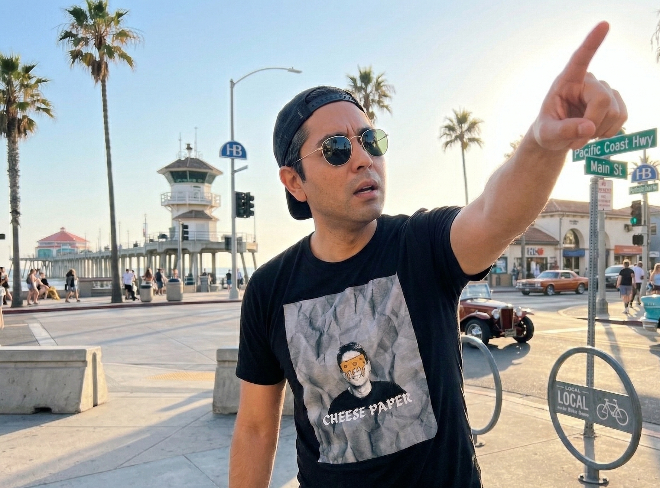 Man pointing towards a street sign with palm trees and a beachfront building in the background
